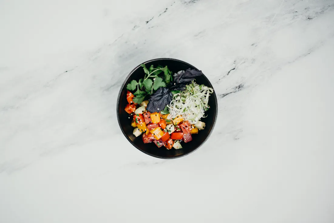Salada com vegetais e folhas em uma tigela preta sobre uma mesa clara